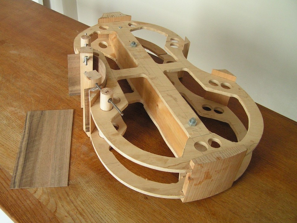 The mould with corner and top and bottom blocks attached and the first rib bent and cramped to shape. The piece of wood to the left is the second rib before bending.